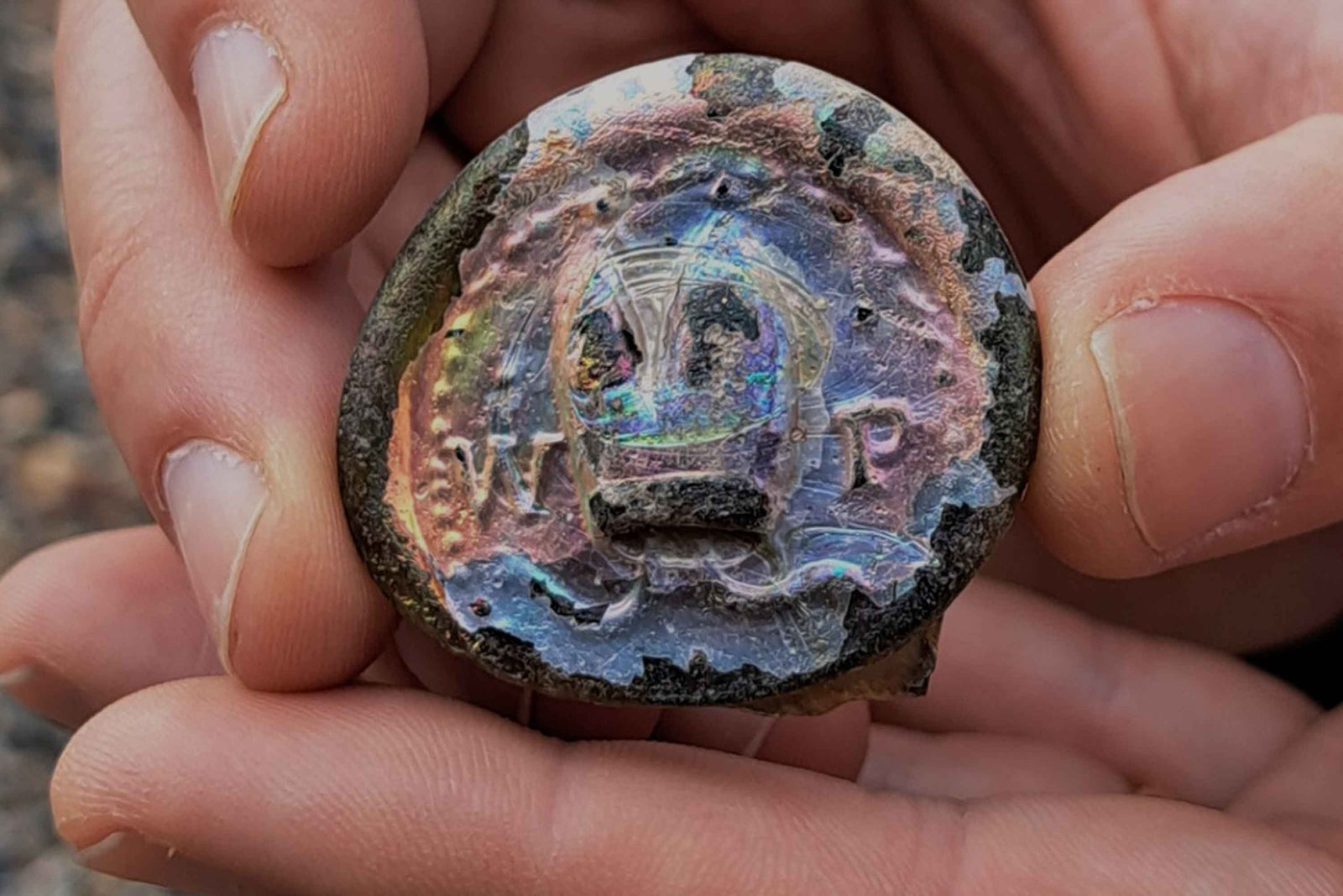 Close up of a person holding a 17th Century wine bottle seal with the initials 'W' and 'P+' either side of a bishop's mitre