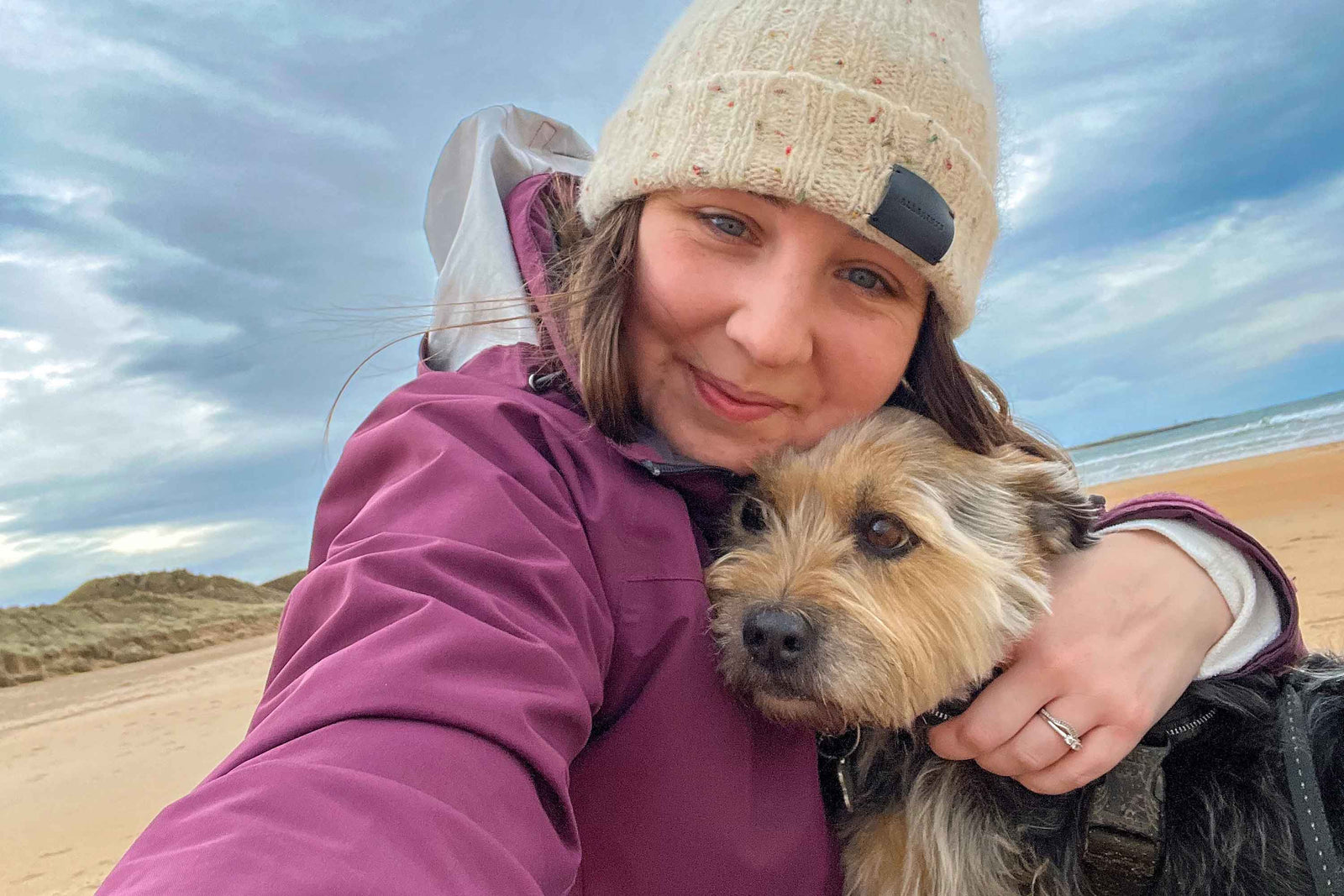 Emily wearing a pink jacket and beanie hat on a beach with her dog Murphy