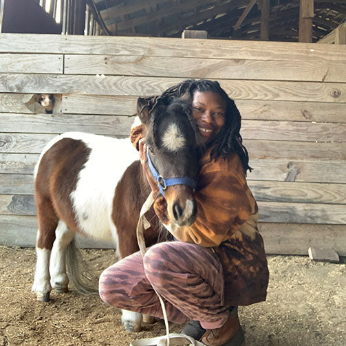 Caitlin Gooch hugging a small pony in a barn