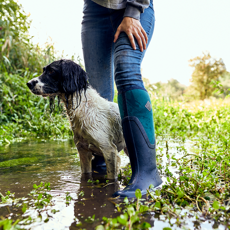 PERSON IN MUDDY BROOK WITH THEIR DOG WEARING MUCK BOOTS