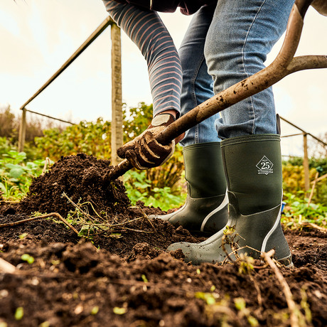 PERSON WEARING GREEN MUCK BOOTS DIGGING UP AN ALLOTMENT FOR GARDENING