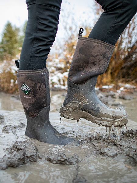 Close up muddy image of a person wearing a pair of Muck Boot Wetland wellingtons
