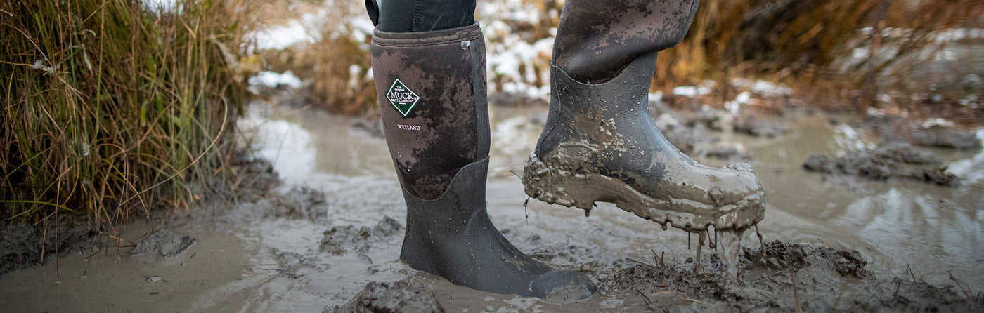 Close up muddy image of a person wearing a pair of Muck Boot Wetland wellingtons