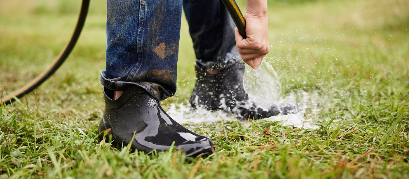 Close up of a person watering grass with a hosepipe, wearing a pair of black Muck Boot Wooster boots
