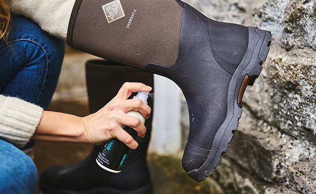 Person applying Grangers Rubber Boot Care Spray to a pair of Muck Boots Derwent II wellingtons