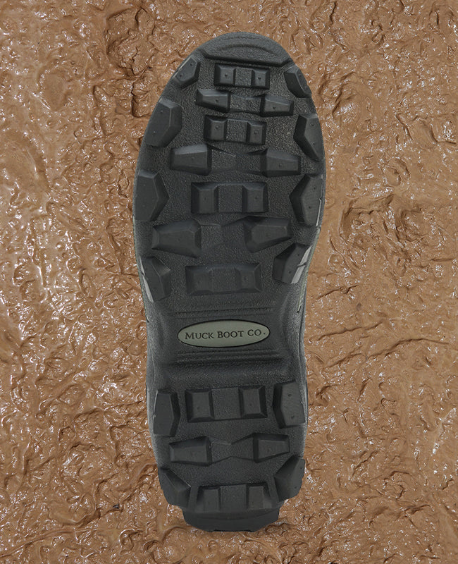 A Muck Boots Muckmaster outsole with a mud texture behind