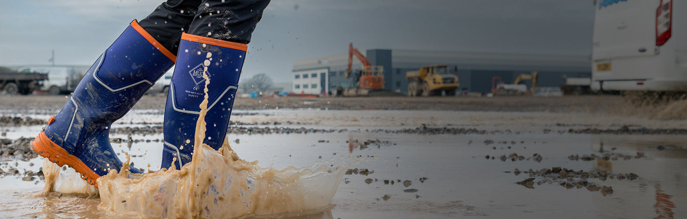 Person walking through a puddle, wearing a pair of blue Muck Boots S5 Grit Wellingtons