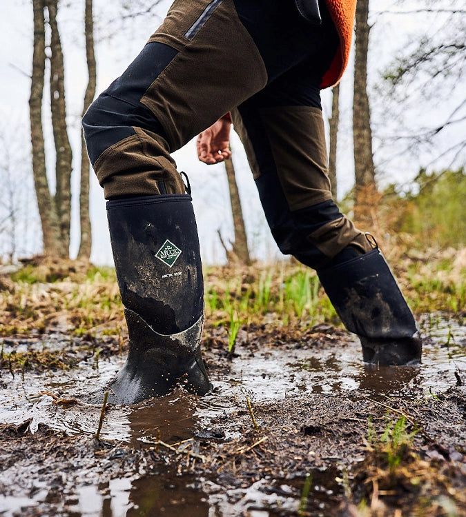Man walking through muddy ground in a pair of Muck Boots