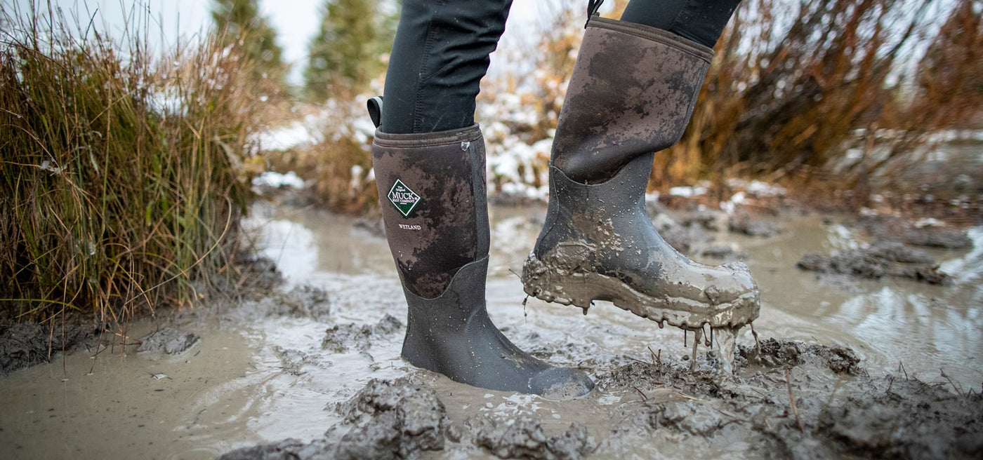 Close-up image of a person wearing a pair of muddy Muck Boots Wetland wellingtons