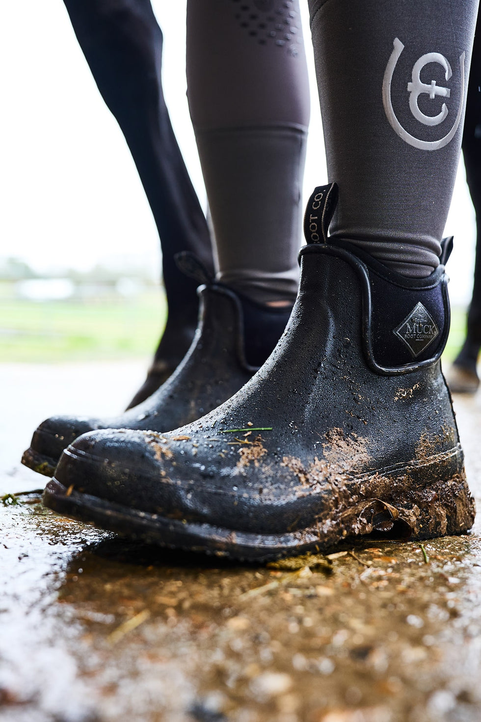Close up image of a person wearing a pair of muddy Muck Boots Unisex Wear Ankle Boots in a horse stable