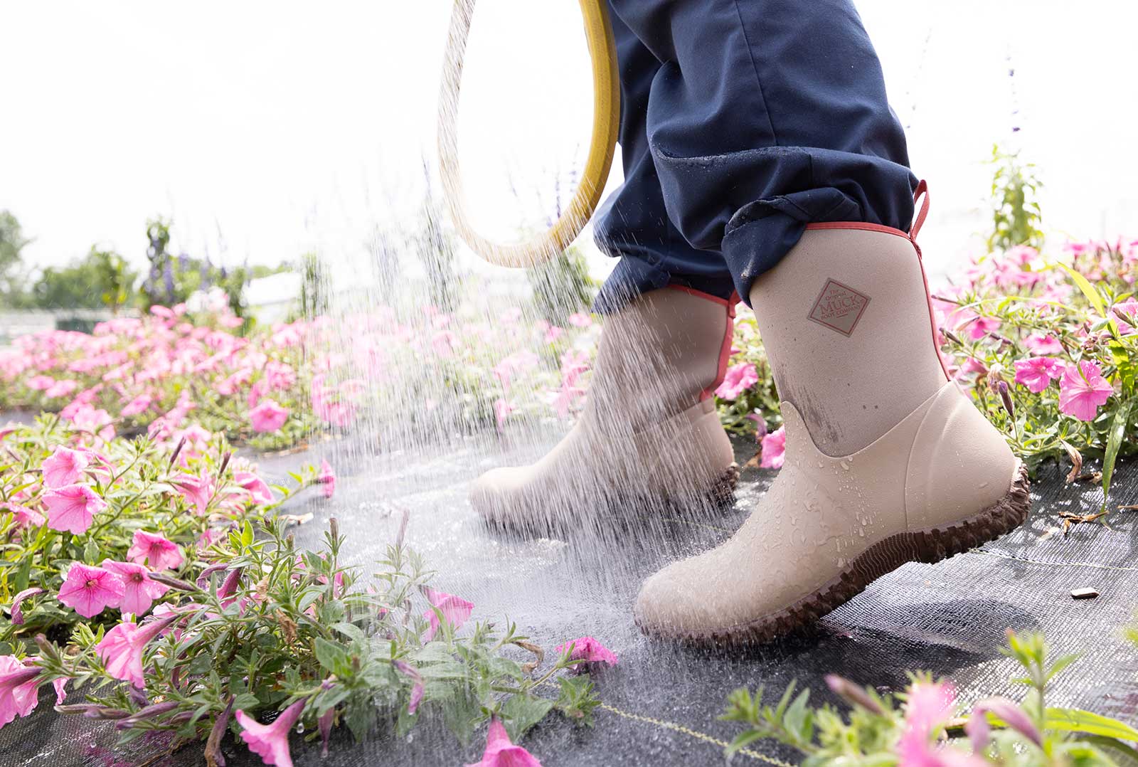 Close up of a person wearing a pair of Salmon pink Muck Boot Muckster II Wellingtons, while watering pink flowers