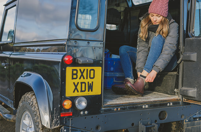 Woman putting on a pair of Muck Boots in the back of a Land Rover