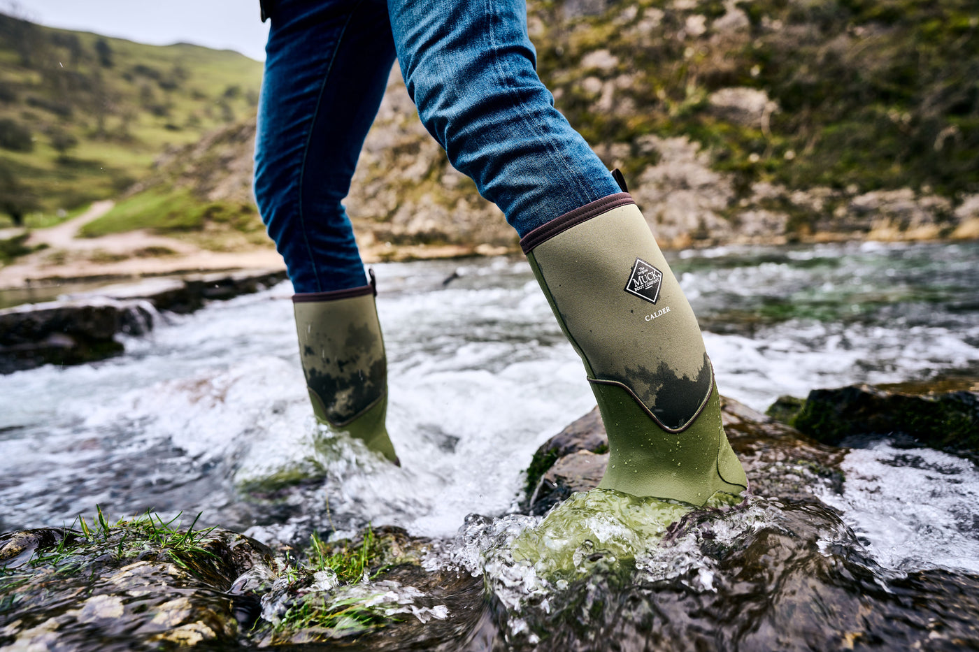 Person walking through a rocky stream, wearing a pair of Muck Boots Calder wellingtons