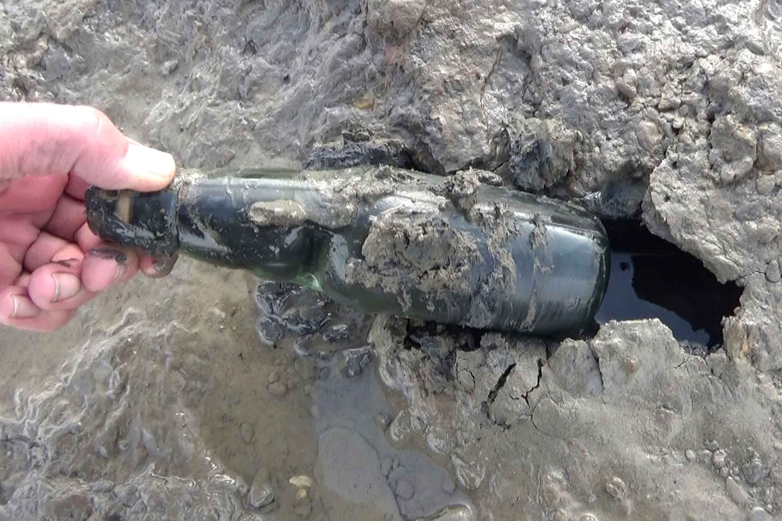 Close up of a hand pulling a bottle out of mud
