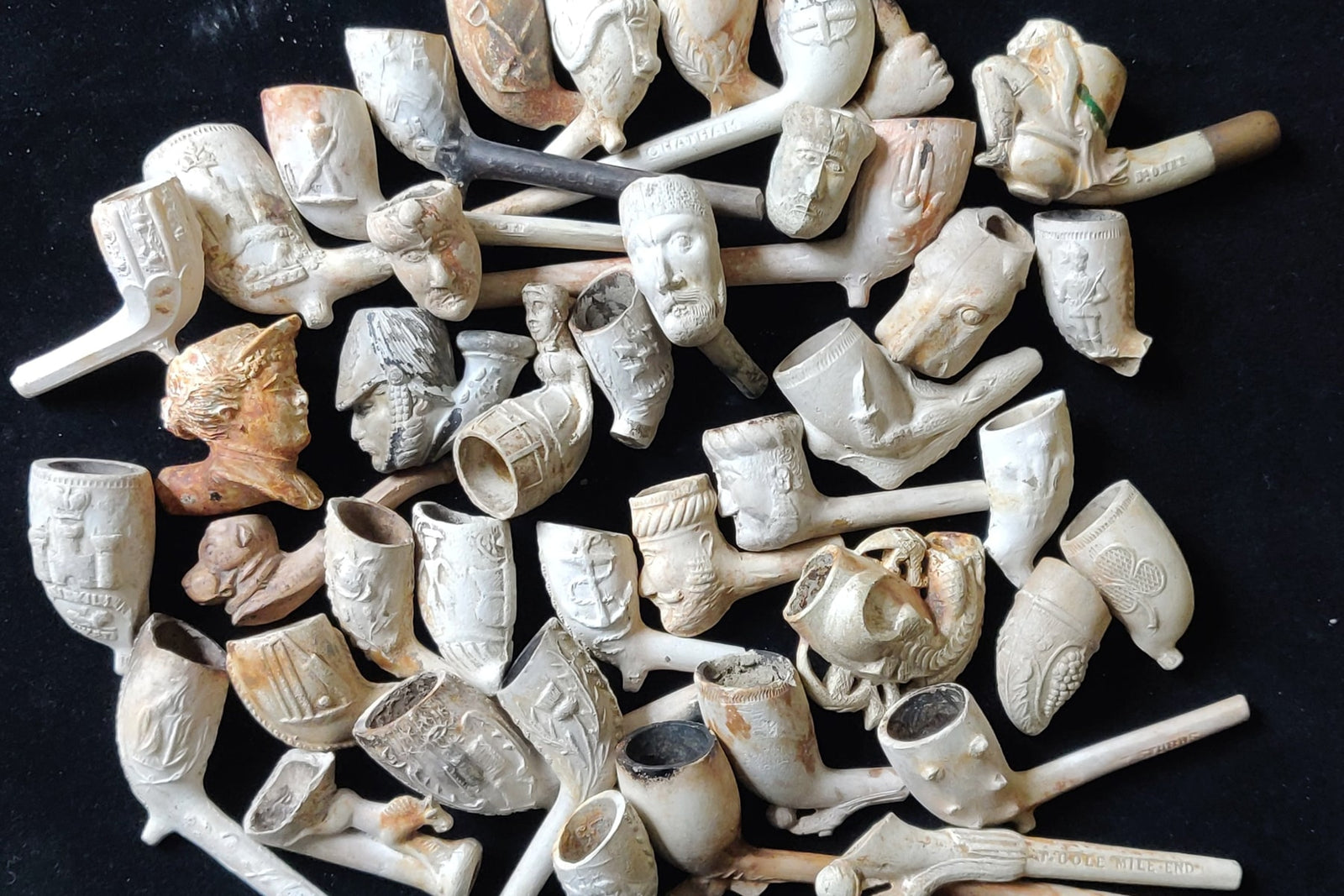 A collection of clay pipe bowls made during the 19th century on a black background