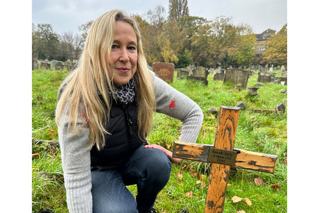 Nicola White in a graveyard crouched down in front of the wooden cross with a brass plaque in memory of Sarah Jury