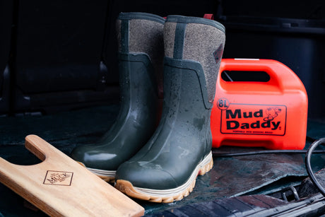 A pair of Muck Boots Women's Arctic Sport II Tall Boots next to a Muck Boots branded boot jack and a can of Mud Daddy cleaning kit.