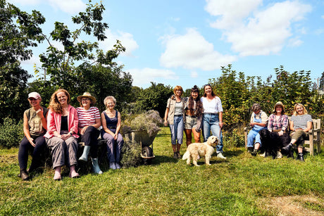 A group of people stood and sat in a green space, all wearing Muck Boots Rainscape Boots with two dogs also present
