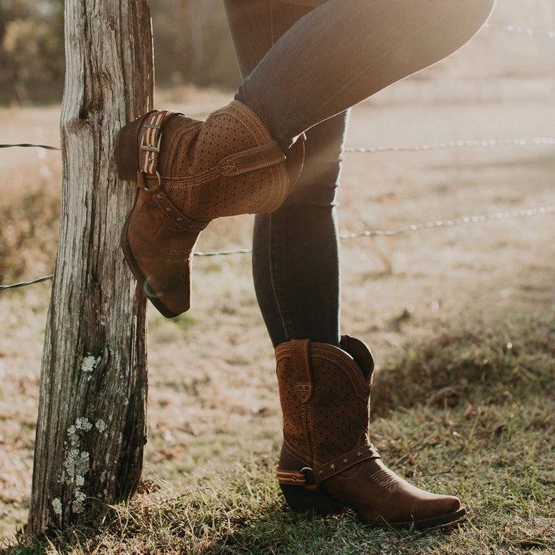 A women stood resting her foot on a fence post, wearing a pair of Durango Women's Crush Western Boots