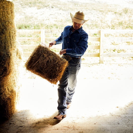 Man carrying a haybale through a barn, wearing a pair of Durango boots