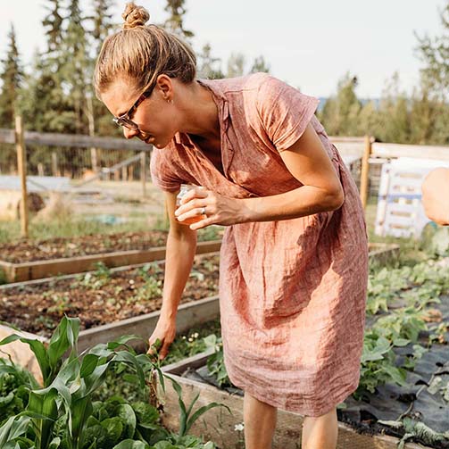 Kate Schat holding a glass and wearing a pink dress in an allotment 