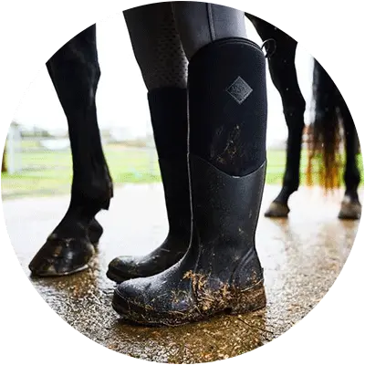Close up image of a person wearing a pair of Muck Boots Colt Ryder Wellingtons inside a horse stable.