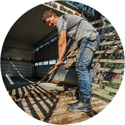 Man wearing a pair of Muck Boots Chore boots cleaning a wooden floor of a horse with a broom.