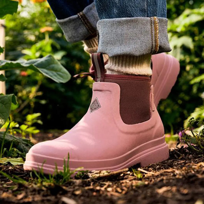 Close-up image of a woman wearing a pair of Muck Boots Women's Rainscape Chelsea Boots in Woodrose Twilight Mauve.