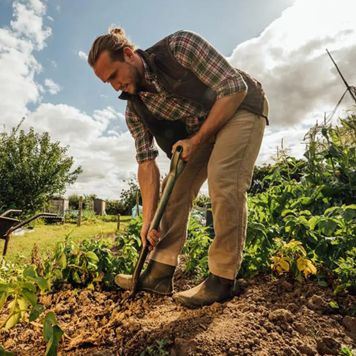 Man wearing a pair of Muck Boots, gardening and digging into earth with a shovel.