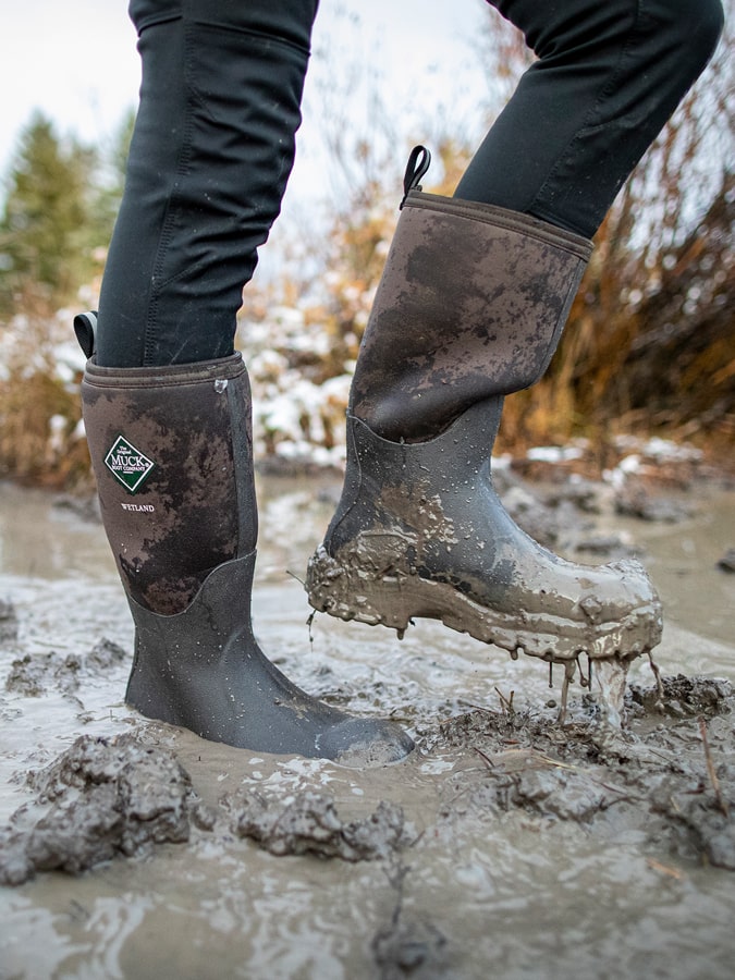 Close-up image of a person wearing a pair of muddy Muck Boots Wetland wellingtons