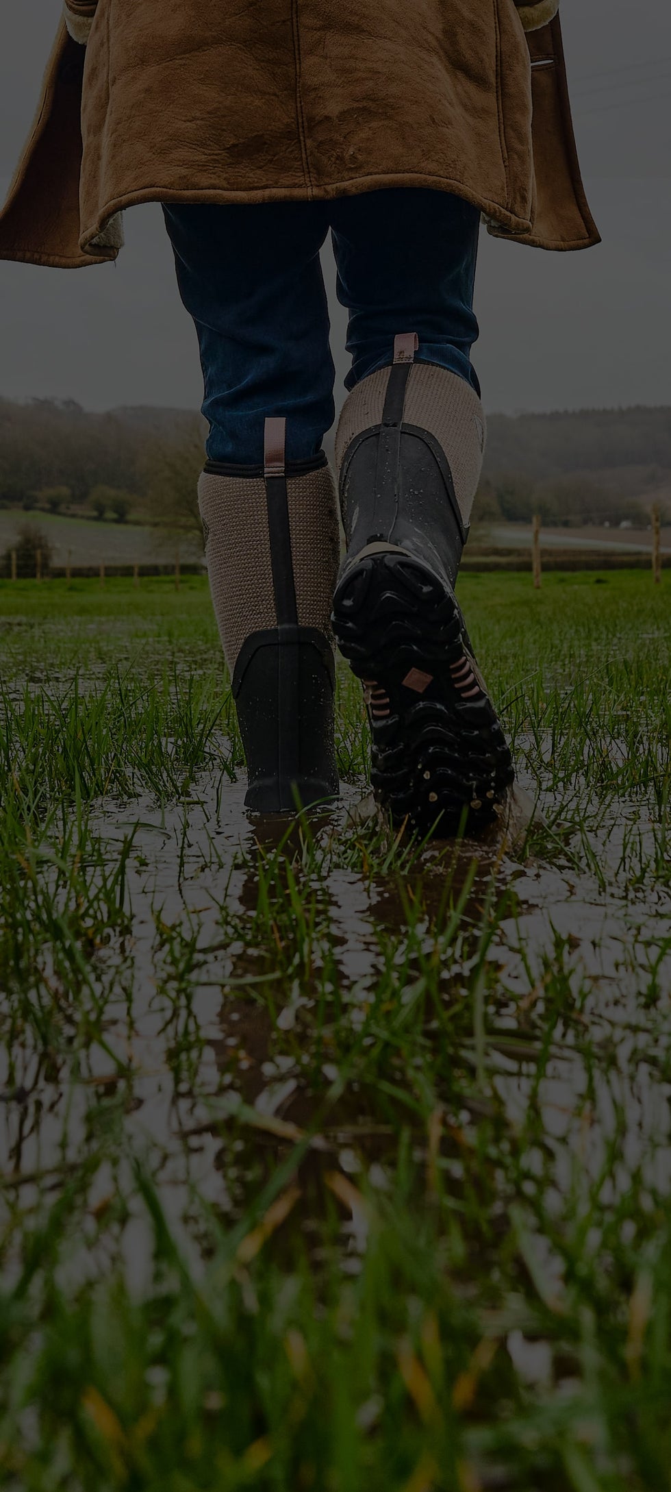 Woman walking through a wet field, wearing a pair of Muck Boots Arctic Sport II Wellingtons