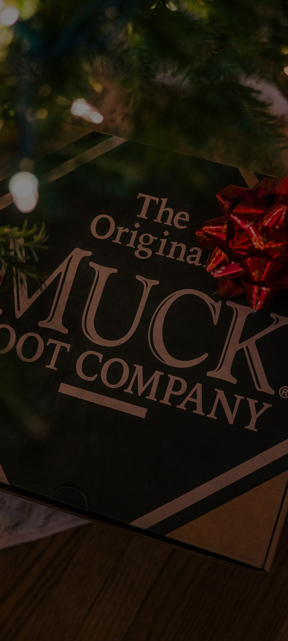 A Muck Boots footwear box with a Christmas gift bow under a Christmas tree