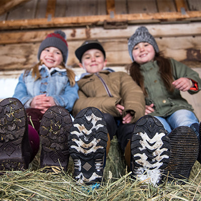 Children sat on a haystack in a barn, wearing Muck Boot wellingtons