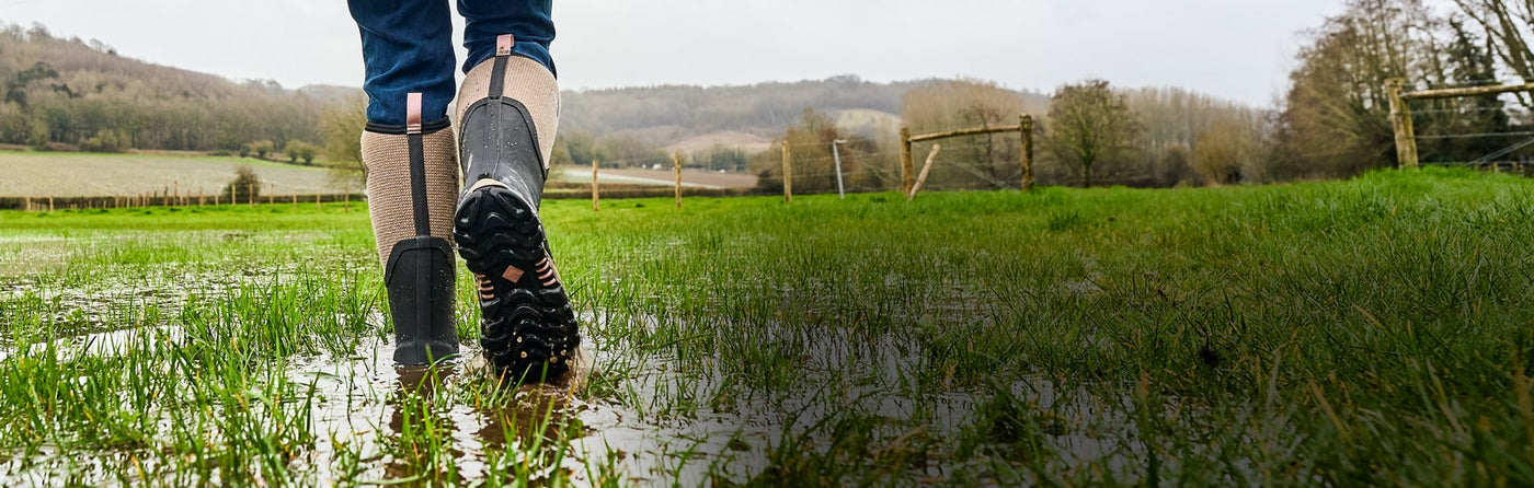 Woman walking through a wet field, wearing a pair of Muck Boots Arctic Sport II Wellingtons