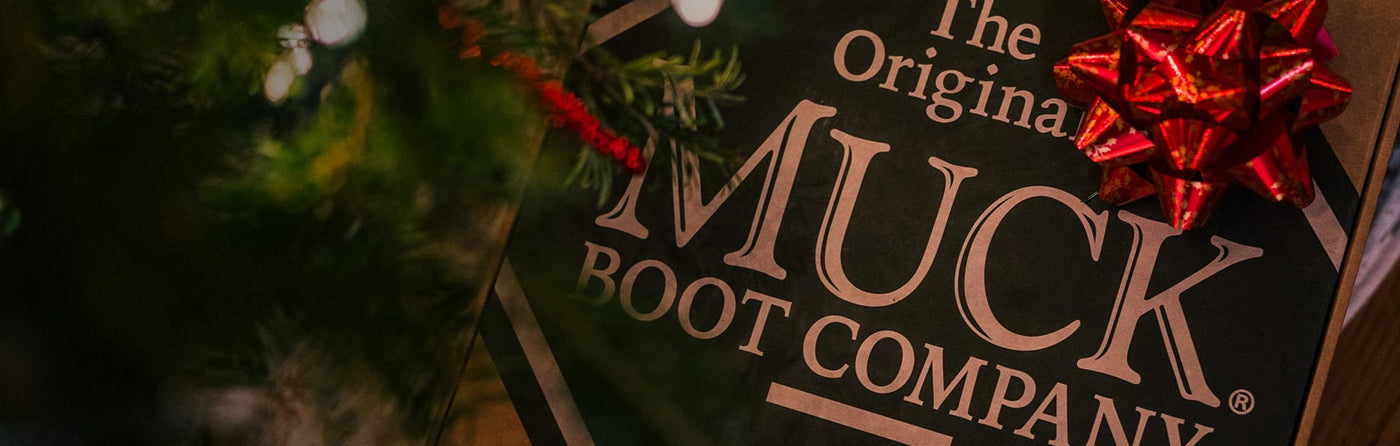 A Muck Boots footwear box with a Christmas gift bow under a Christmas tree