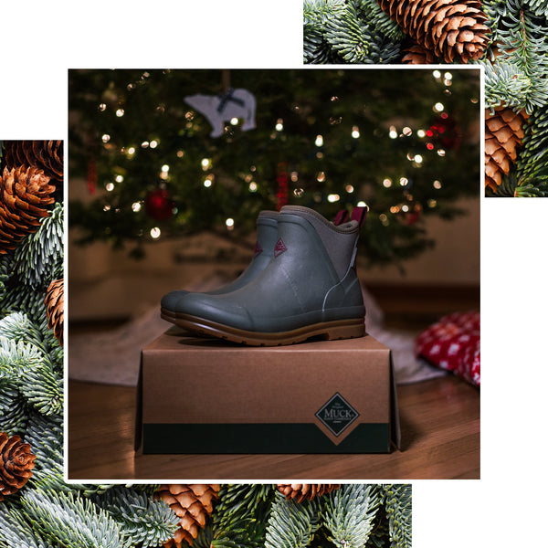 A pair of Muck Boots Muck Originals boots on a box with a Christmas tree behind with a pine tree texture border around the image