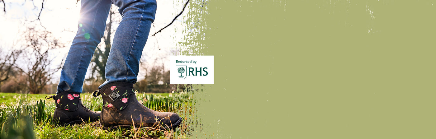 Woman stood amongst spring flowers in bloom, wearing a pair of Muck Boots 