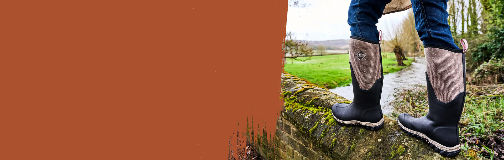 Close-up image of a woman wearing a pair of Muck Boots Women's Arctic Sport II Tall Boots while walking along a moss covered bridge wall.