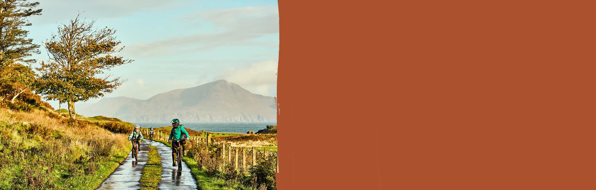 A mother and two children out riding bikes along a lane with a lake and mountain back-drop.