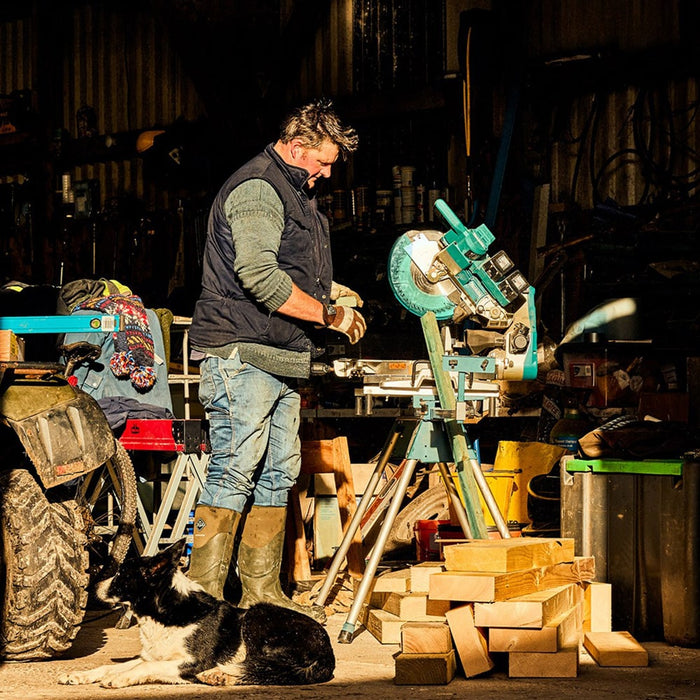 A male builder in an open workshop, wearing a pair of Muck Boots with a border collie dog lying in front of him