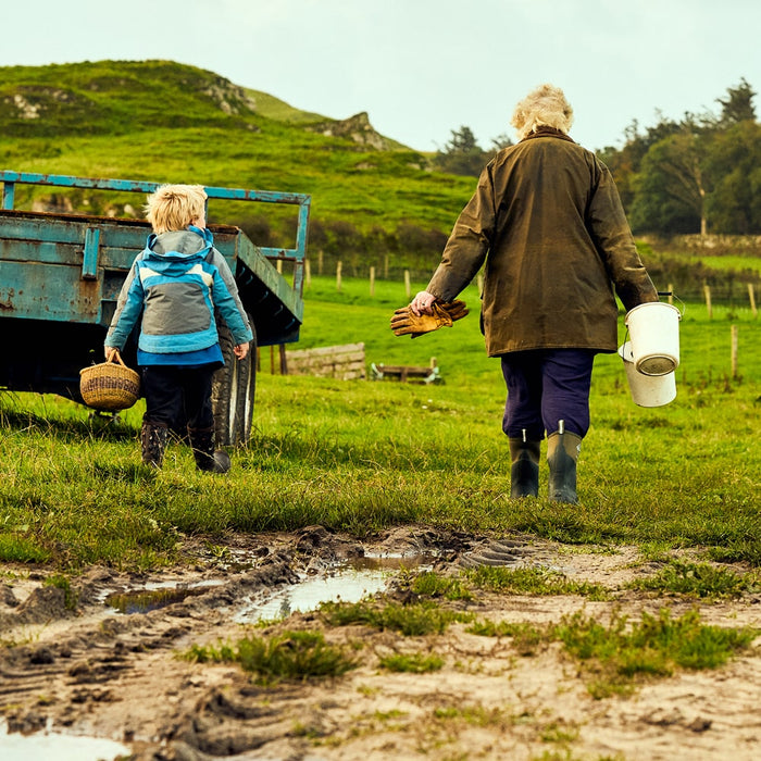 Woman and child walking through muddy farmland, wearing Muck Boots and carrying buckets, gloves and a basket