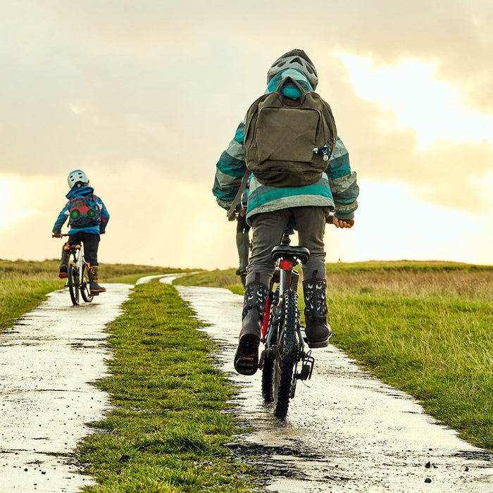 Two children wearing Muck Boots wellingtons, riding their push bikes along a country lane