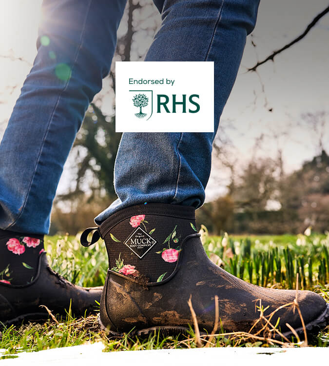 Woman stood amongst spring flowers in bloom, wearing a pair of Muck Boots 