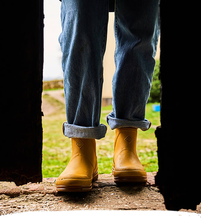 Person stood in a doorway, wearing a pair of yellow Muck Boots Muck Original boots.