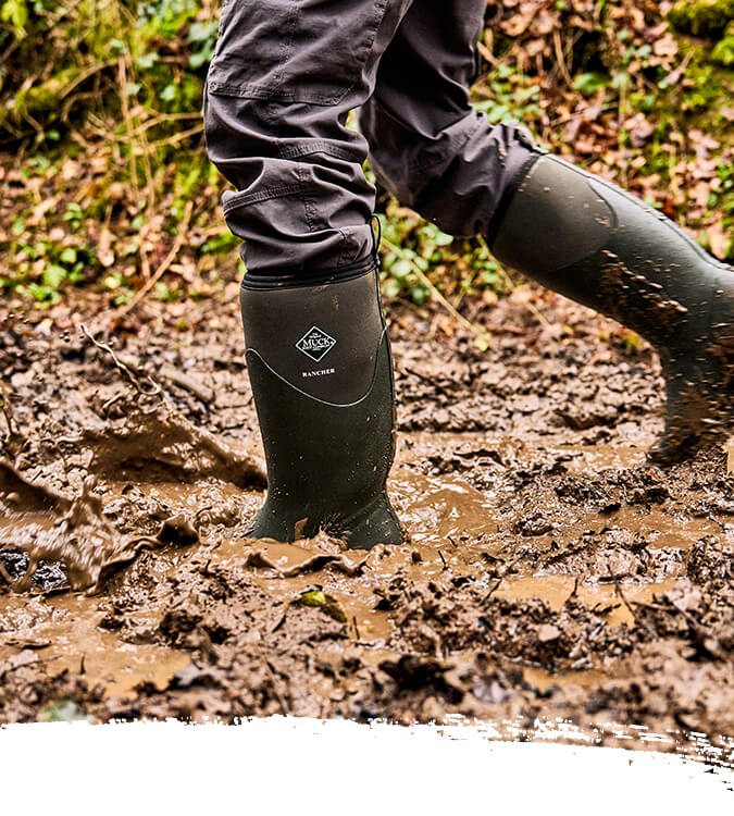 Person wearing a pair of green Muck Boots Rancher wellington boots walking through a muddy field