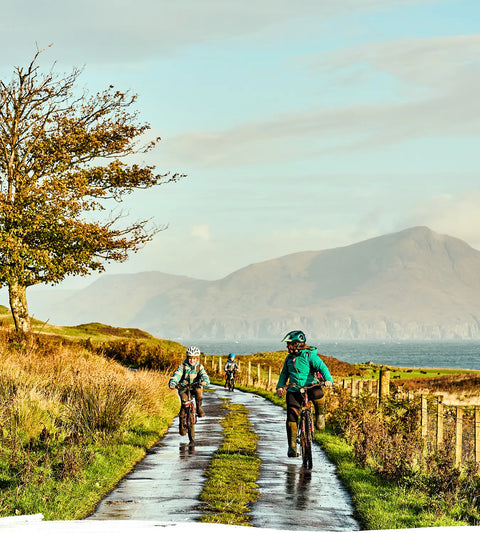 A mother and two children out riding bikes along a lane with a lake and mountain back-drop.