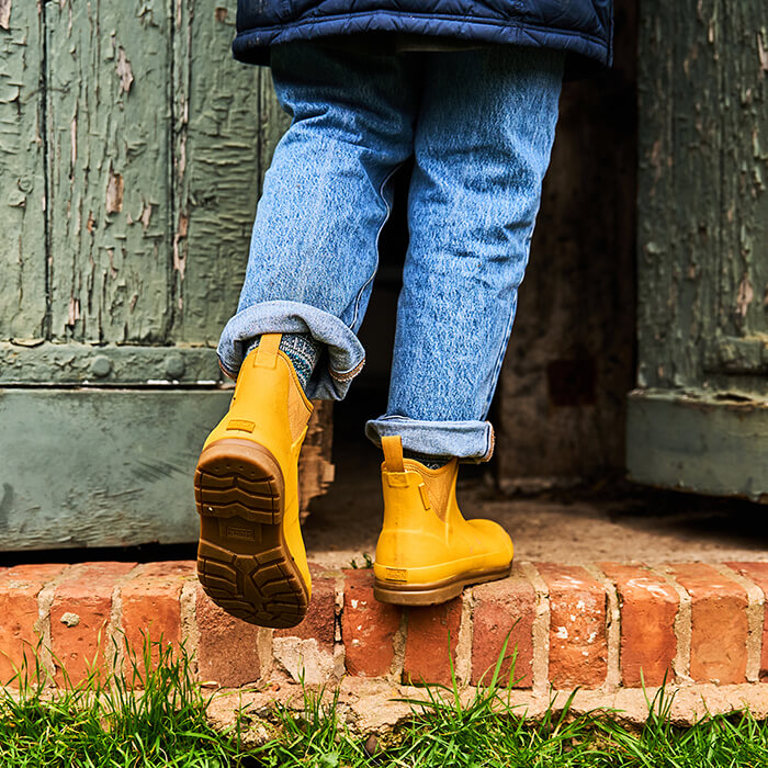 Close-up image of a woman walking up a brick step, wearing a pair of yellow Muck Boots Muck Originals Boots