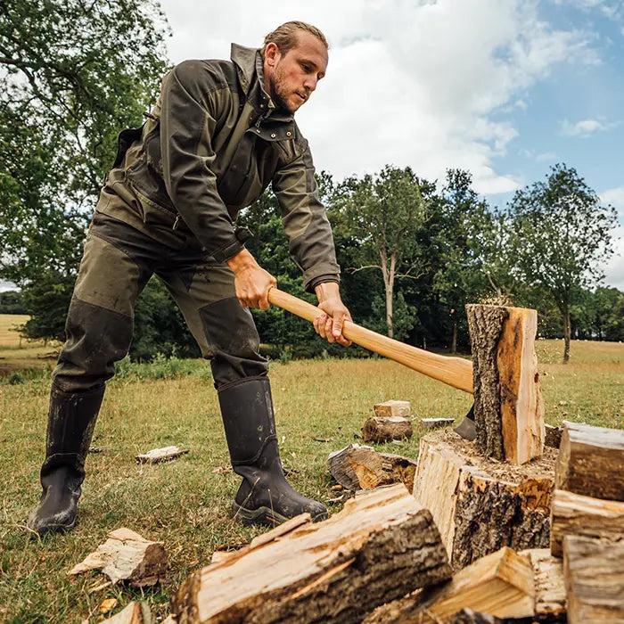 A man chopping wood outside wearing a pair of Muck Boots Wetland Wellingtons.