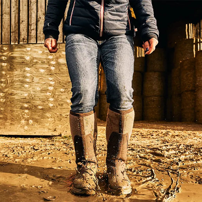 A woman stood in mud wearing a pair of Muck Boots Arctic Sport II Wellingtons