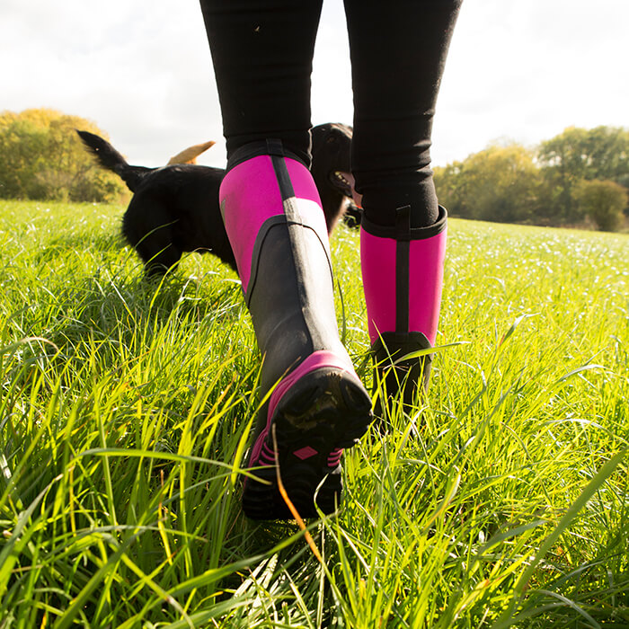 Close-up image of a woman wearing a pair of pink Arctic Sport II Tall Boots with a black dog in the grass
